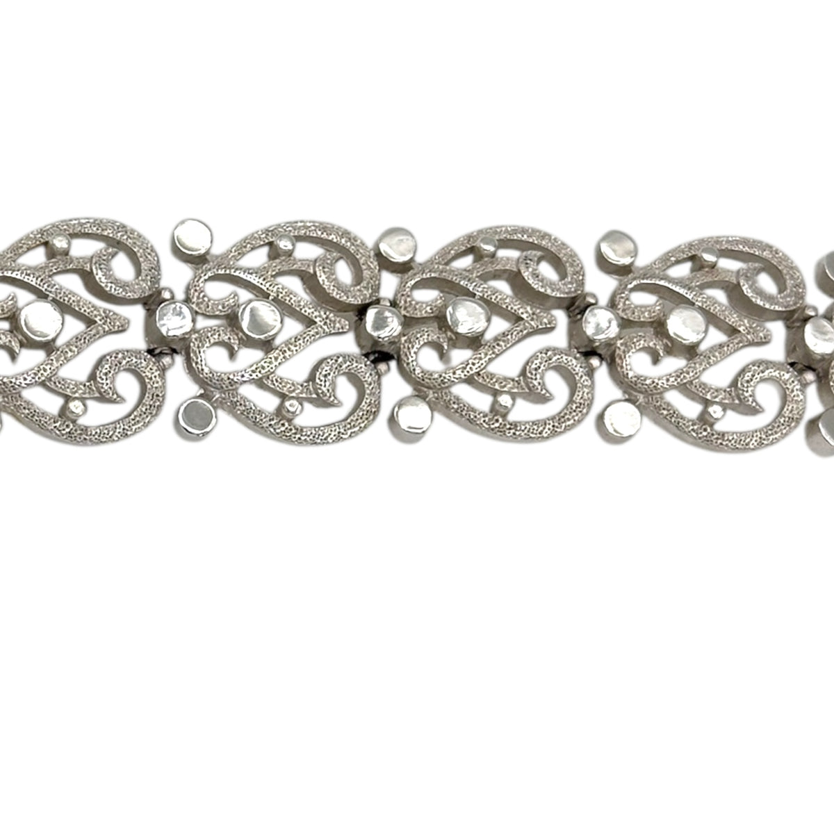 Close up view of the links of Trifari silver-tone vintage bracelet featuring filigree scroll links and beaded accents on white background.