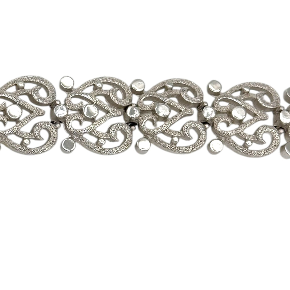 Close up view of the links of Trifari silver-tone vintage bracelet featuring filigree scroll links and beaded accents on white background.