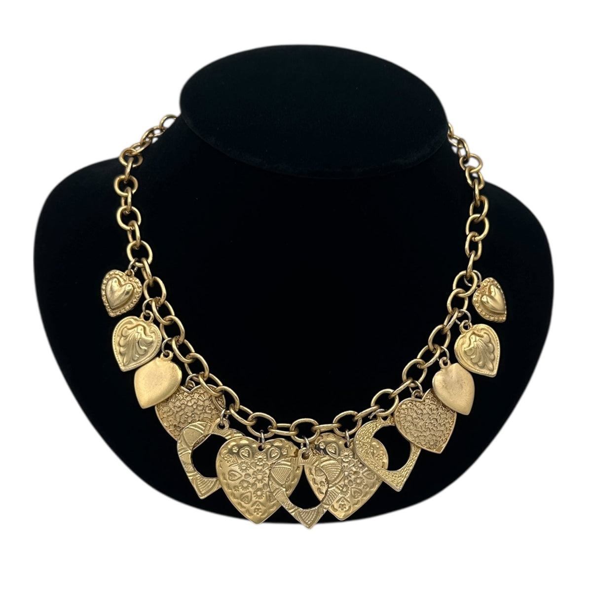 Close up view of Vintage gold heart charm necklace with textured hearts and link chain displayed on black velvet bust.