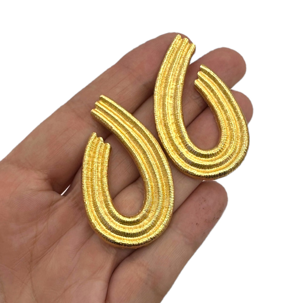 Vintage Givenchy gold teardrop dangle earrings with textured finish displayed on hand on white background.