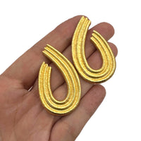Vintage Givenchy gold teardrop dangle earrings with textured finish displayed on hand on white background.