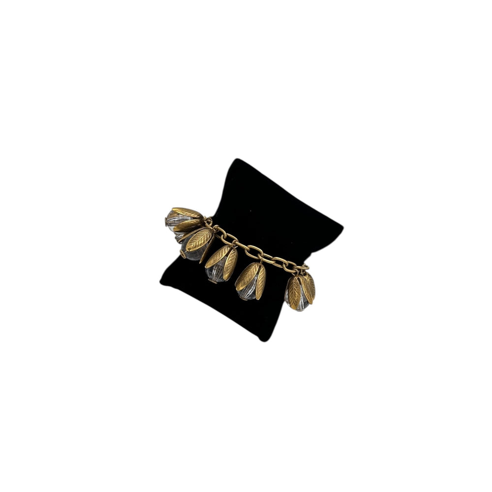Gold bracelet with leaf-like designs on a black velvet stand against a white background