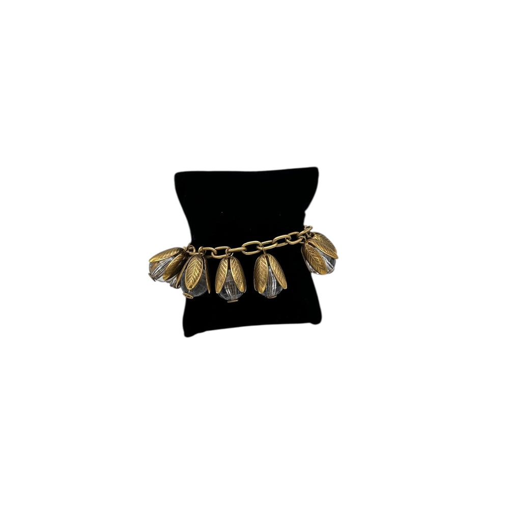 Gold bracelet with leaf-like designs on a black jewelry stand against a white background