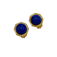 Close up of Vintage Ciner gold clip-on earrings with round blue lapis glass cabochons displayed on white background.