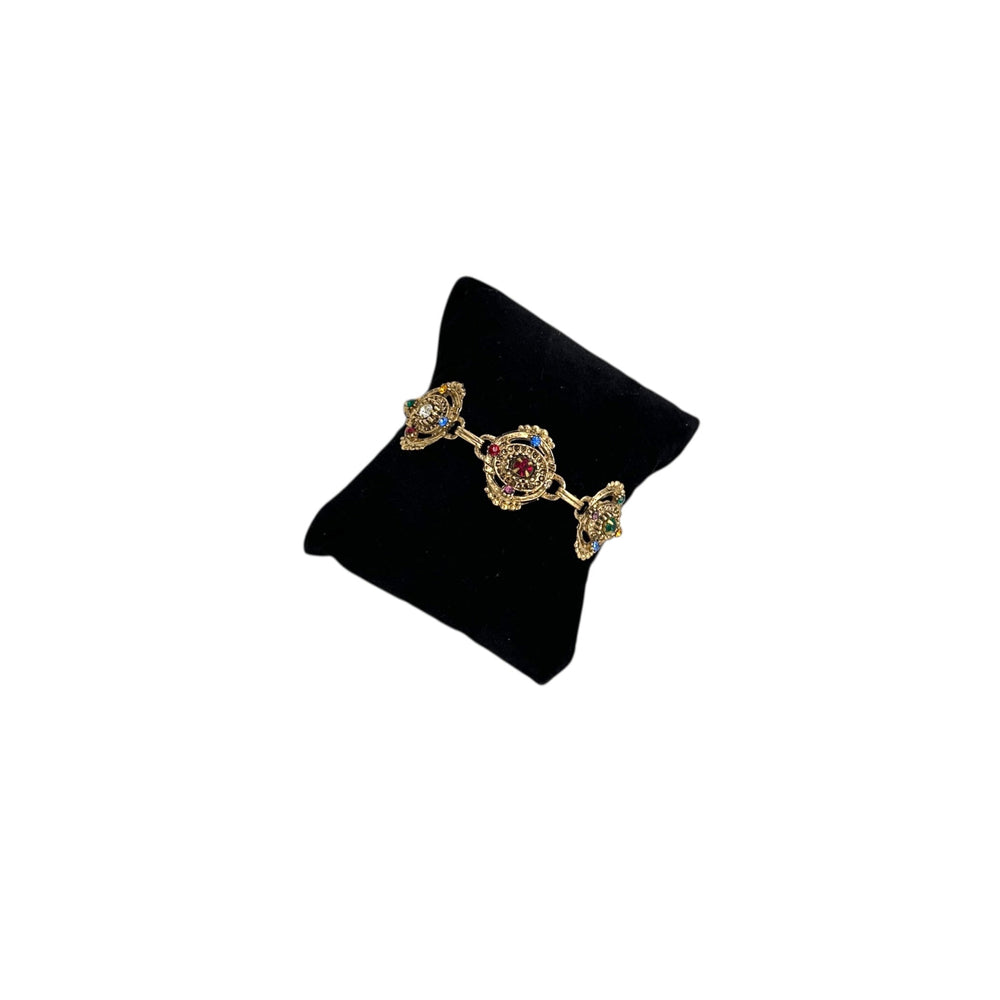 Coro vintage gold tone filigree bracelet featuring multi-color rhinestones and intricate mid-century detailing on black pillow.