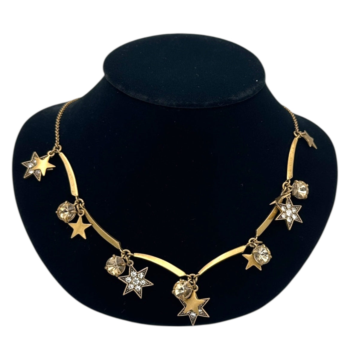 Close up view of J. Crew vintage antiqued gold star charm necklace with rhinestone accents displayed on a black jewelry bust.