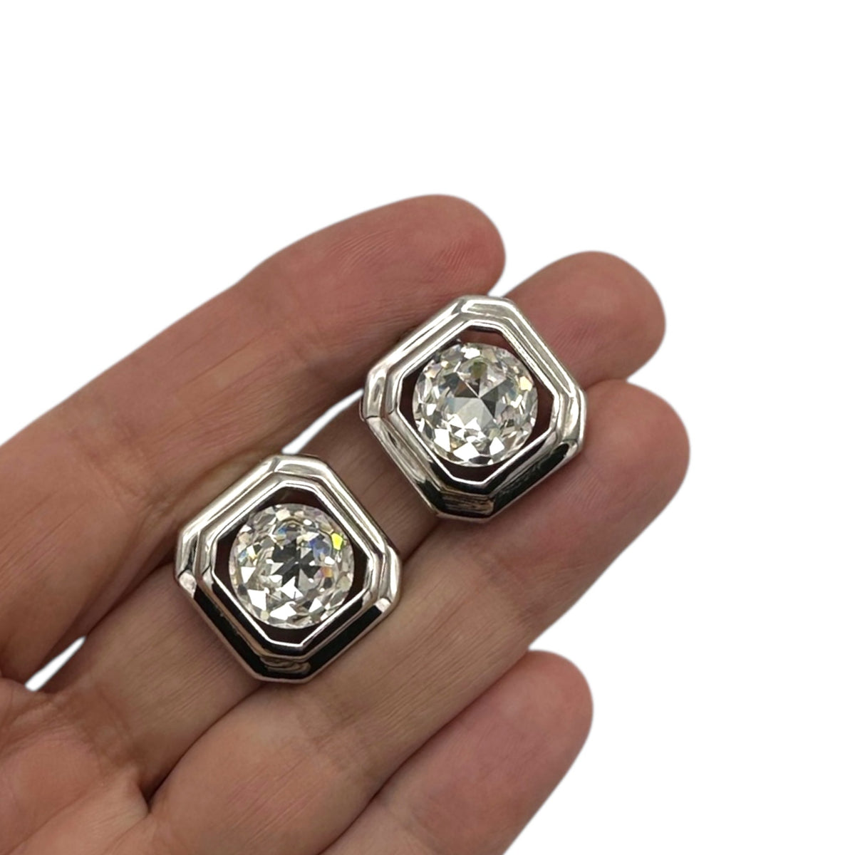 Shown on hand, Vintage Joan Rivers silver clear rhinestone clip-on earring set on white background.
