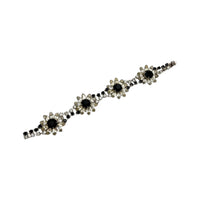 Laying flat, Kirks Folly vintage bracelet with clear and black rhinestone flower design on white background.