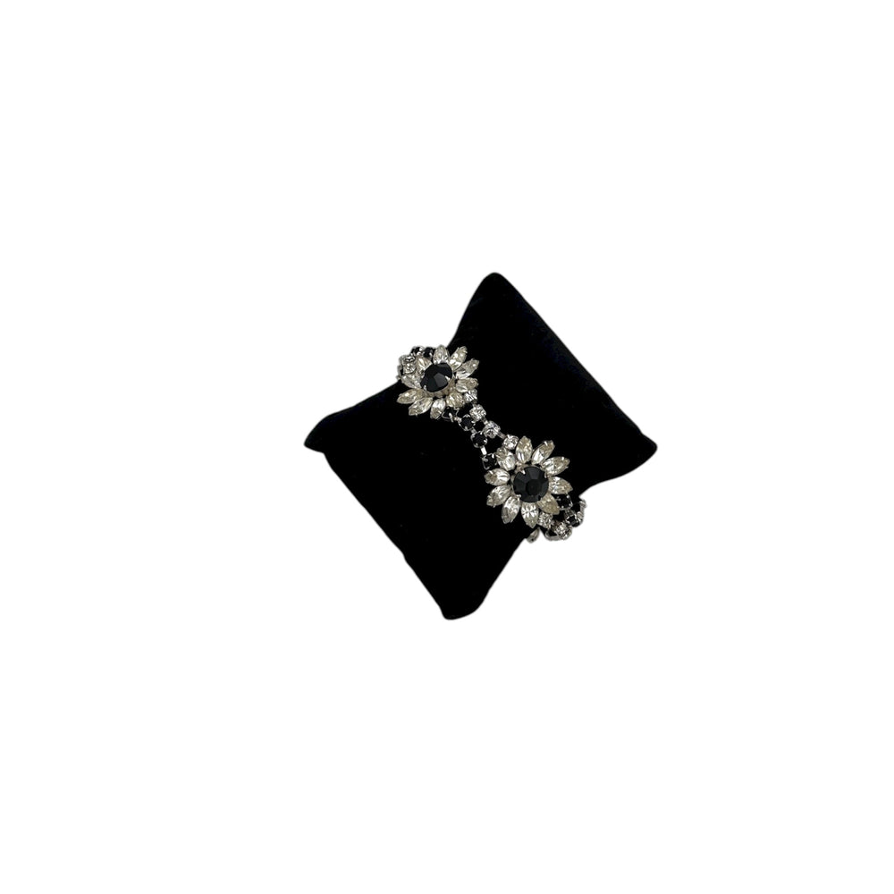 Side view of Kirks Folly vintage bracelet with clear and black rhinestone flower design on back pillow and white background.
