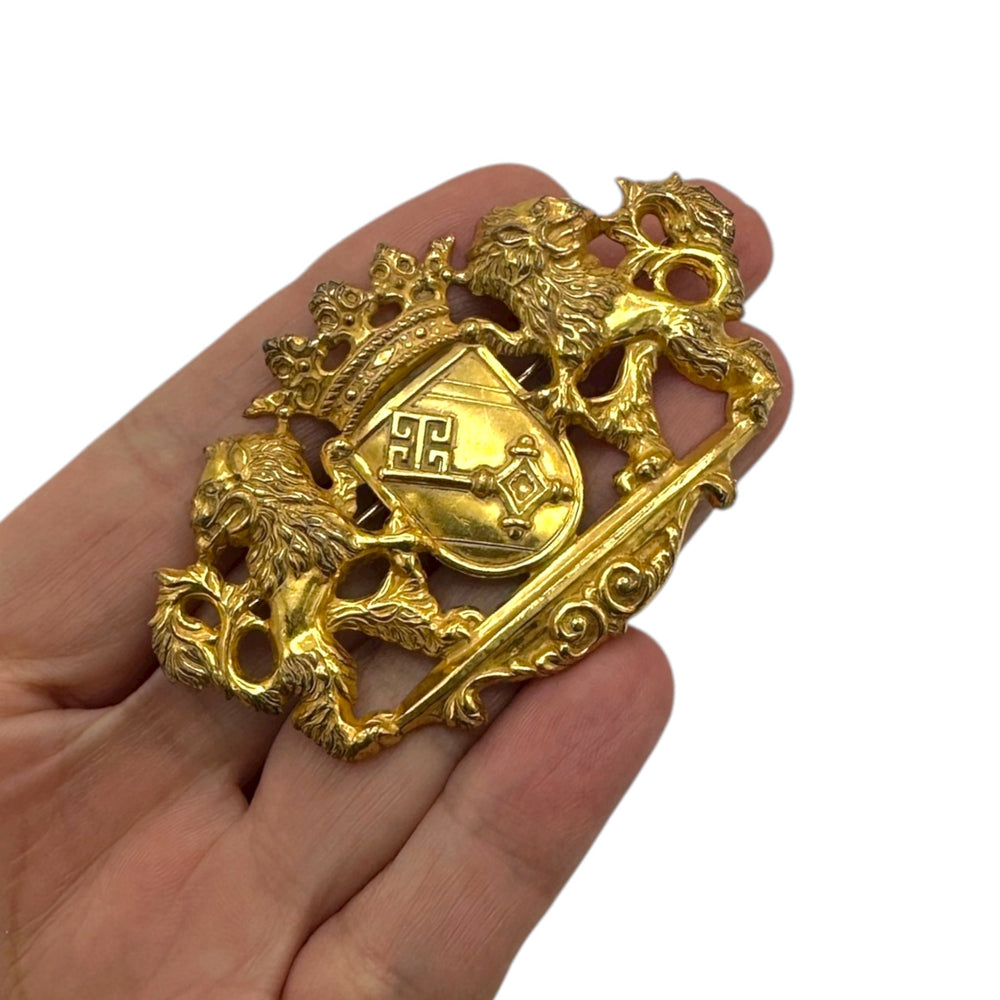Shown on hand to show size, Miriam Haskell gold lion crest vintage brooch with crown and coat of arms design on white background.