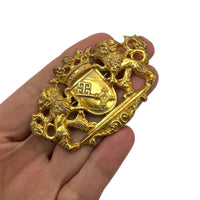 Shown on hand to show size, Miriam Haskell gold lion crest vintage brooch with crown and coat of arms design on white background.