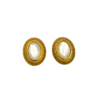 Close up view of Monet vintage gold oval clip-on earrings with opalescent cabochon centers and textured gold frame on white background.