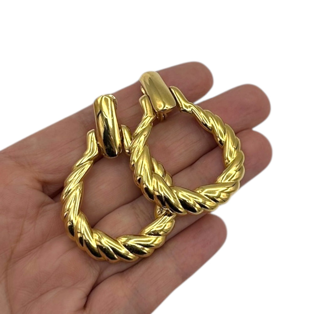 On hand to show size, Monet vintage gold twisted swirl doorknocker clip-on earrings displayed on white background.
