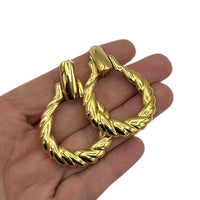 On hand to show size, Monet vintage gold twisted swirl doorknocker clip-on earrings displayed on white background.