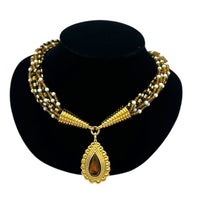 Close up view of Monet vintage gold multi-strand beaded necklace with a brown teardrop pendant and gold accents on a black bust with white background.