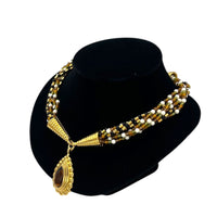 Side view of Monet vintage gold multi-strand beaded necklace with a brown teardrop pendant and gold accents on a black bust with white background.