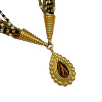 Close up of pendant of Monet vintage gold multi-strand beaded necklace with a brown teardrop pendant and gold accents on white background.