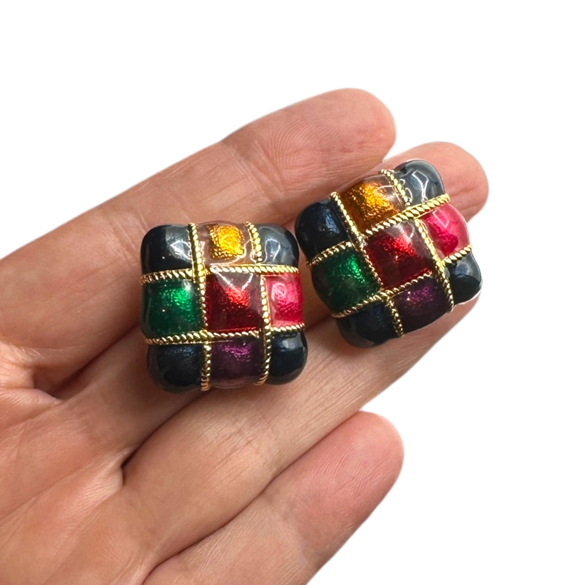 Shown on hand to show size of Vintage Premier Design jewel-tone enamel clip-on earrings with gold grid design in red, green, and amber colors – 1980s statement jewelry shown on white background.