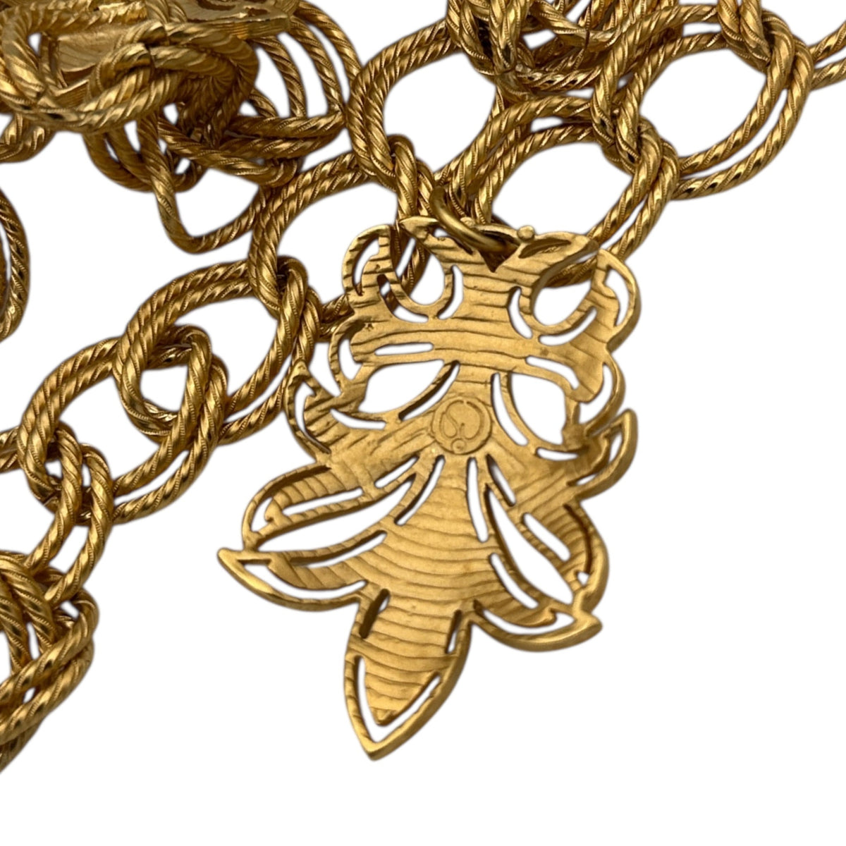 Close up of back view of dangle of Vintage St. John matte gold layered bib belt with ornate leaf accents and curb chain design displayed on white background.