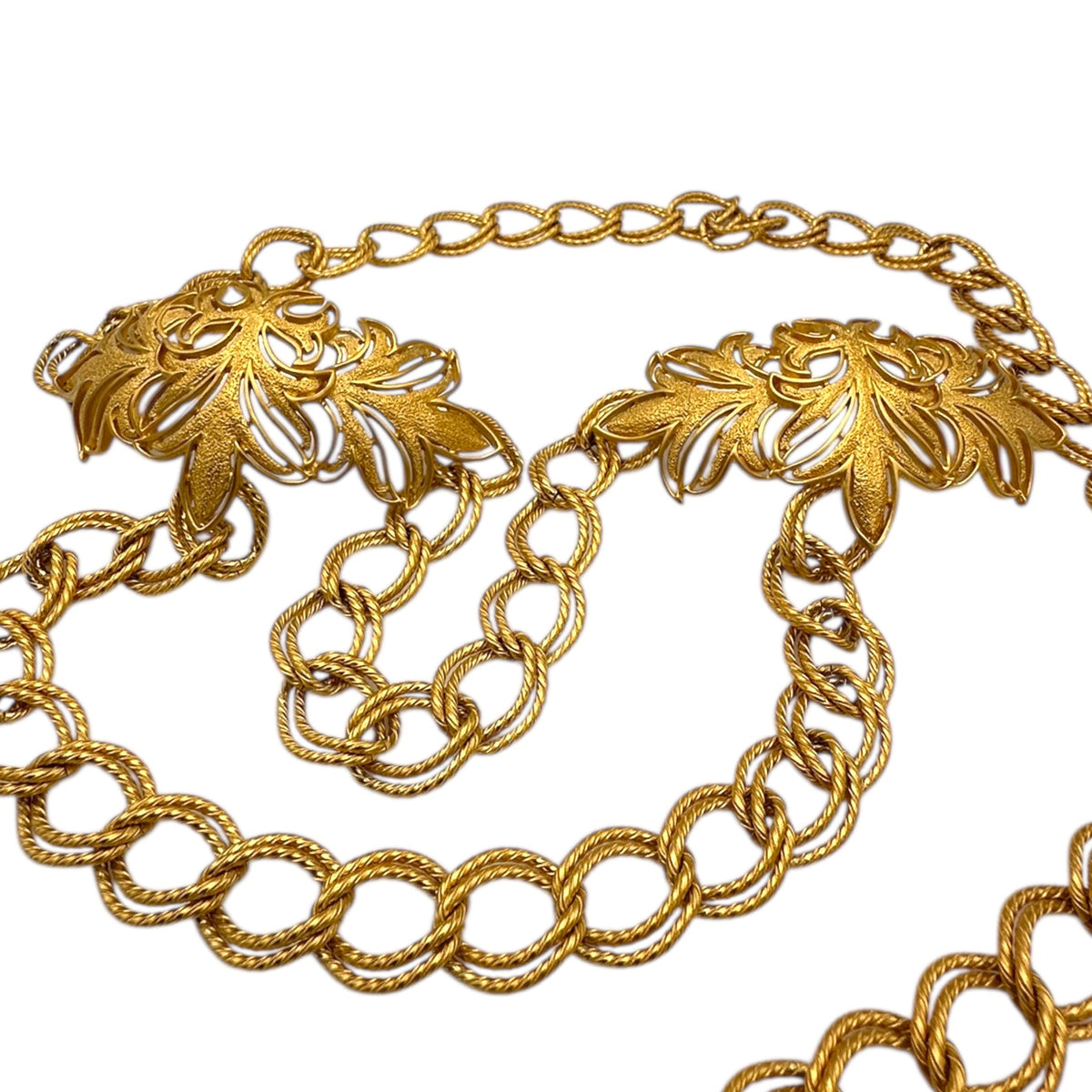 Close up view of the bib of Vintage St. John matte gold layered bib belt with ornate leaf accents and curb chain design displayed on white background.