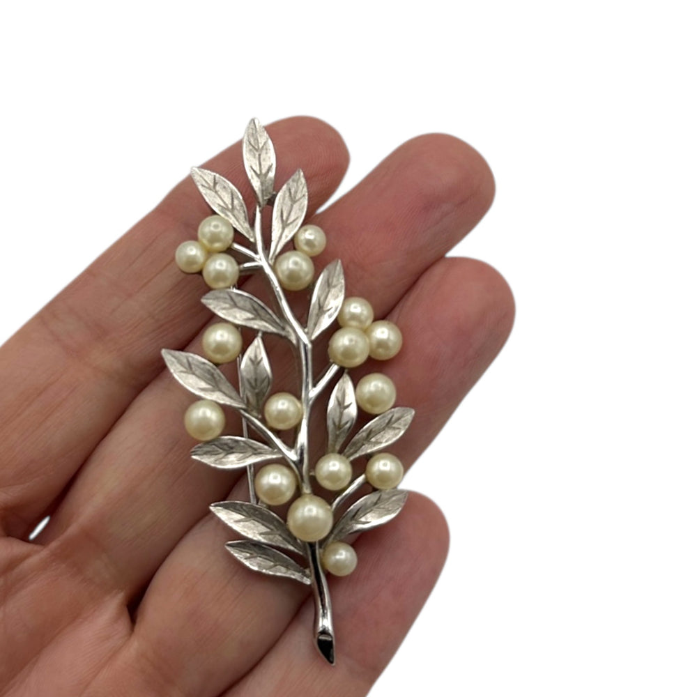 Shown on hand for size, Vintage Trifari silver leaf and pearl brooch with branch design displayed on white background.