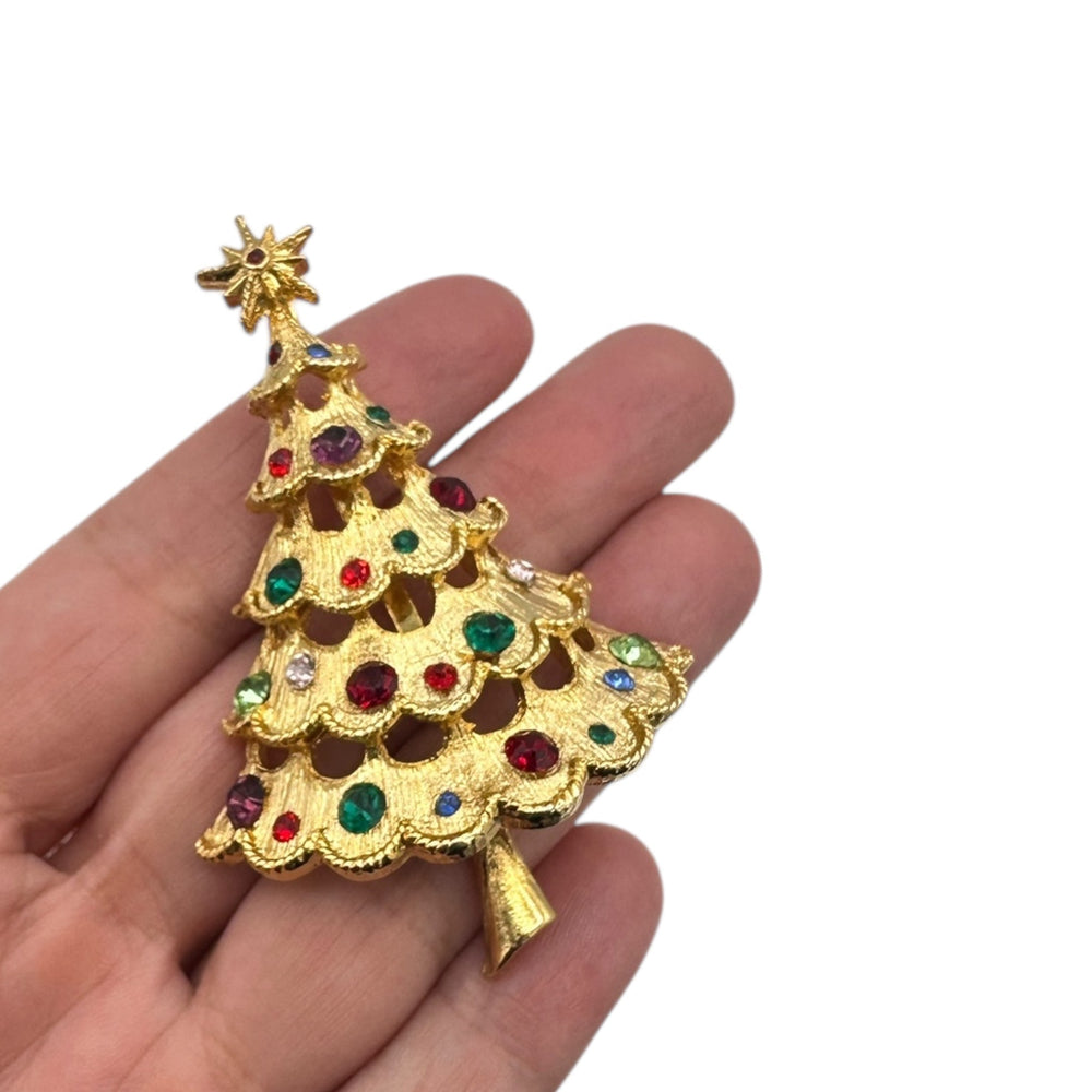 On hand to show size, Ultra Craft vintage gold Christmas tree brooch with multicolor rhinestones and star topper on white background.