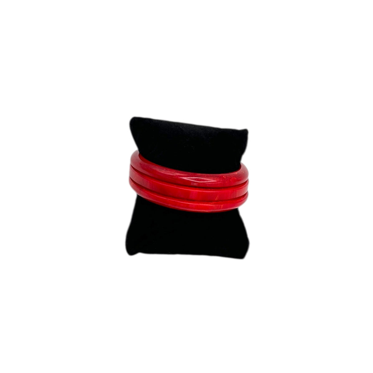 Front view of Set of three vintage cherry red Bakelite bangles stacked on black display pillow, glossy Art Deco style.