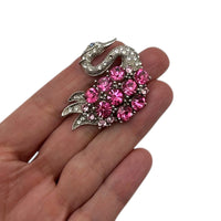 Displayed on hand for size, Vintage silver swan brooch with large round pink rhinestones on white background.