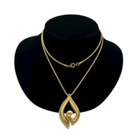Close up view of Vintage Trifari gold modernist pendant necklace on long snake chain on black bust.