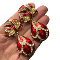 Shown on hand to show size of Whiting & Davis vintage red enamel bow and teardrop rhinestone dangle clip-on earrings, gold-tone statement jewelry on white background.