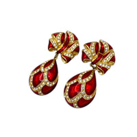 Side view of Whiting & Davis vintage red enamel bow and teardrop rhinestone dangle clip-on earrings, gold-tone statement jewelry on white background.