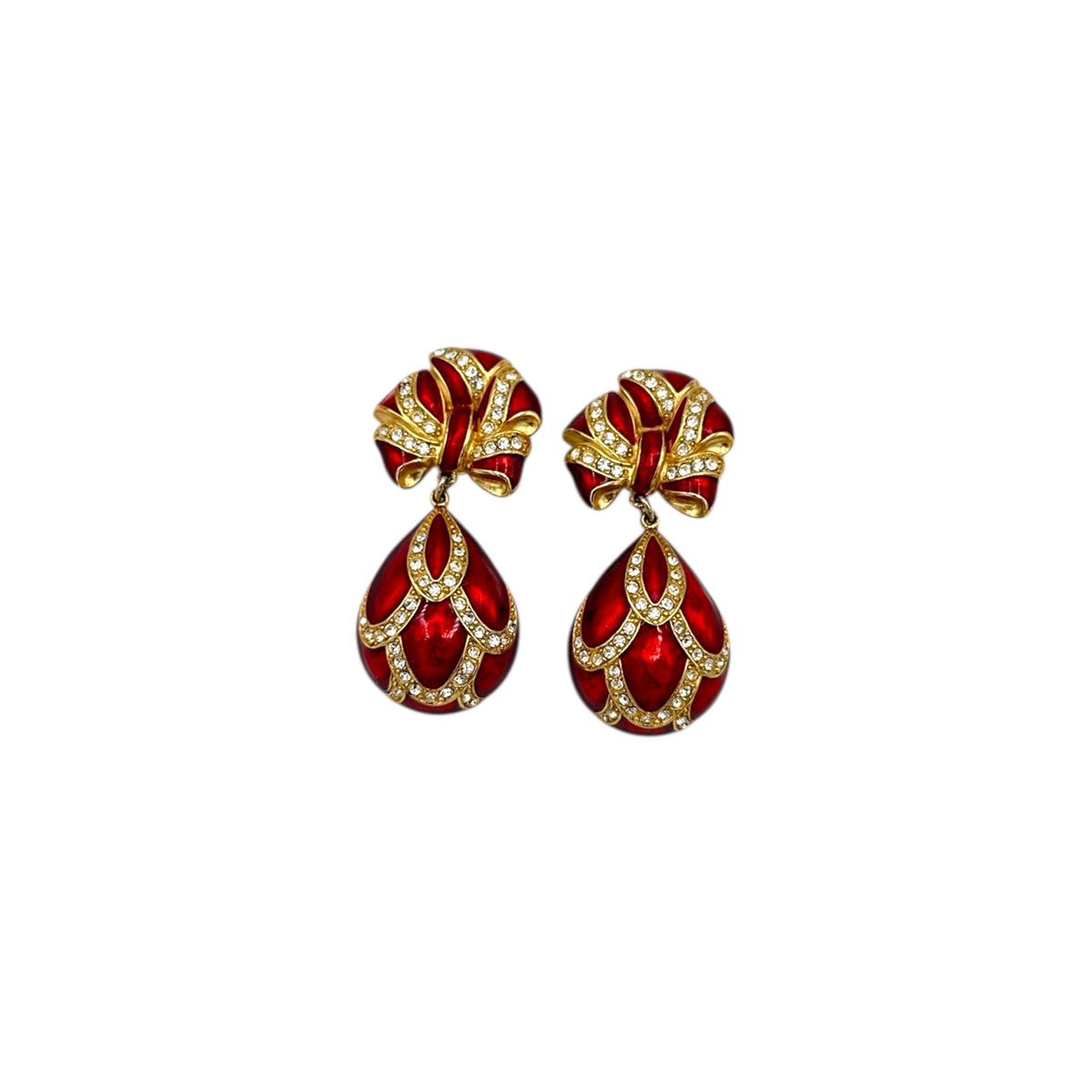 Close up view of Whiting & Davis vintage red enamel bow and teardrop rhinestone dangle clip-on earrings, gold-tone statement jewelry on white background.